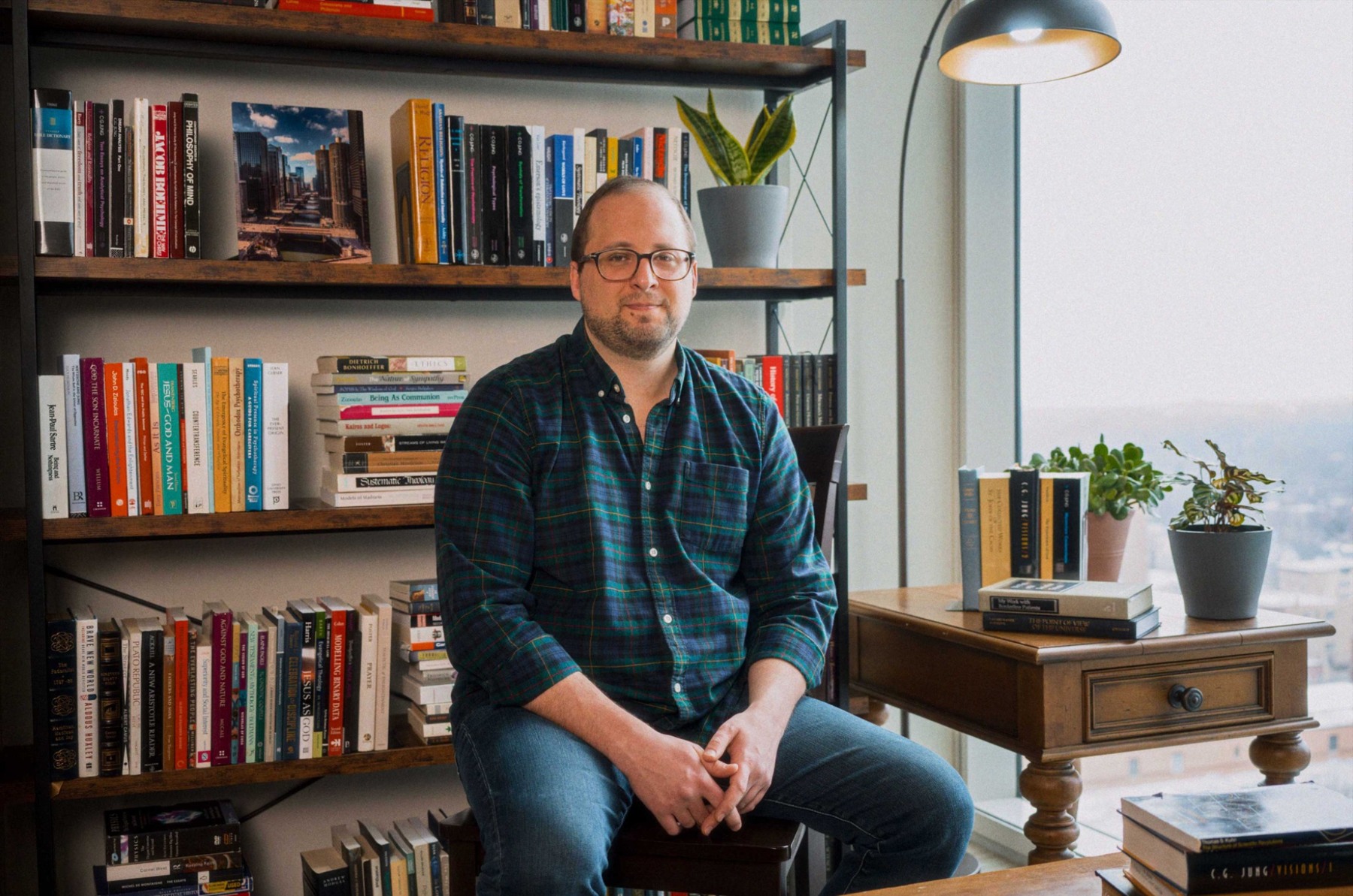 A man seated beside bookshelves and a desk in a home interior
