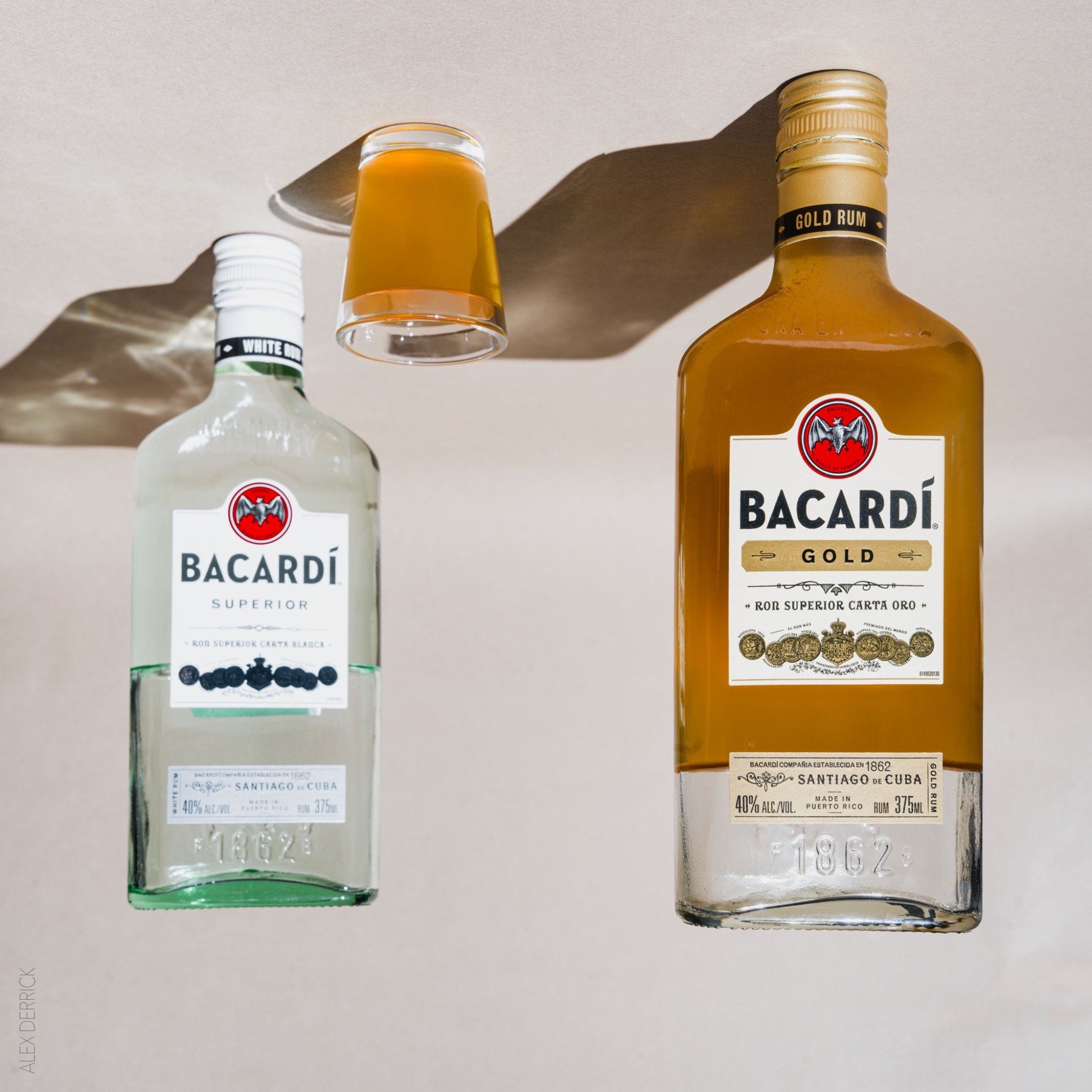 Bacardi rum bottles and a hand holding a glass against a neutral background