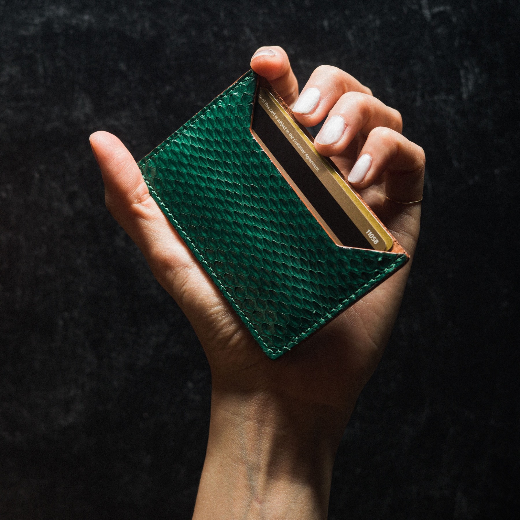 A hand holding a green textured leather card holder against a dark background