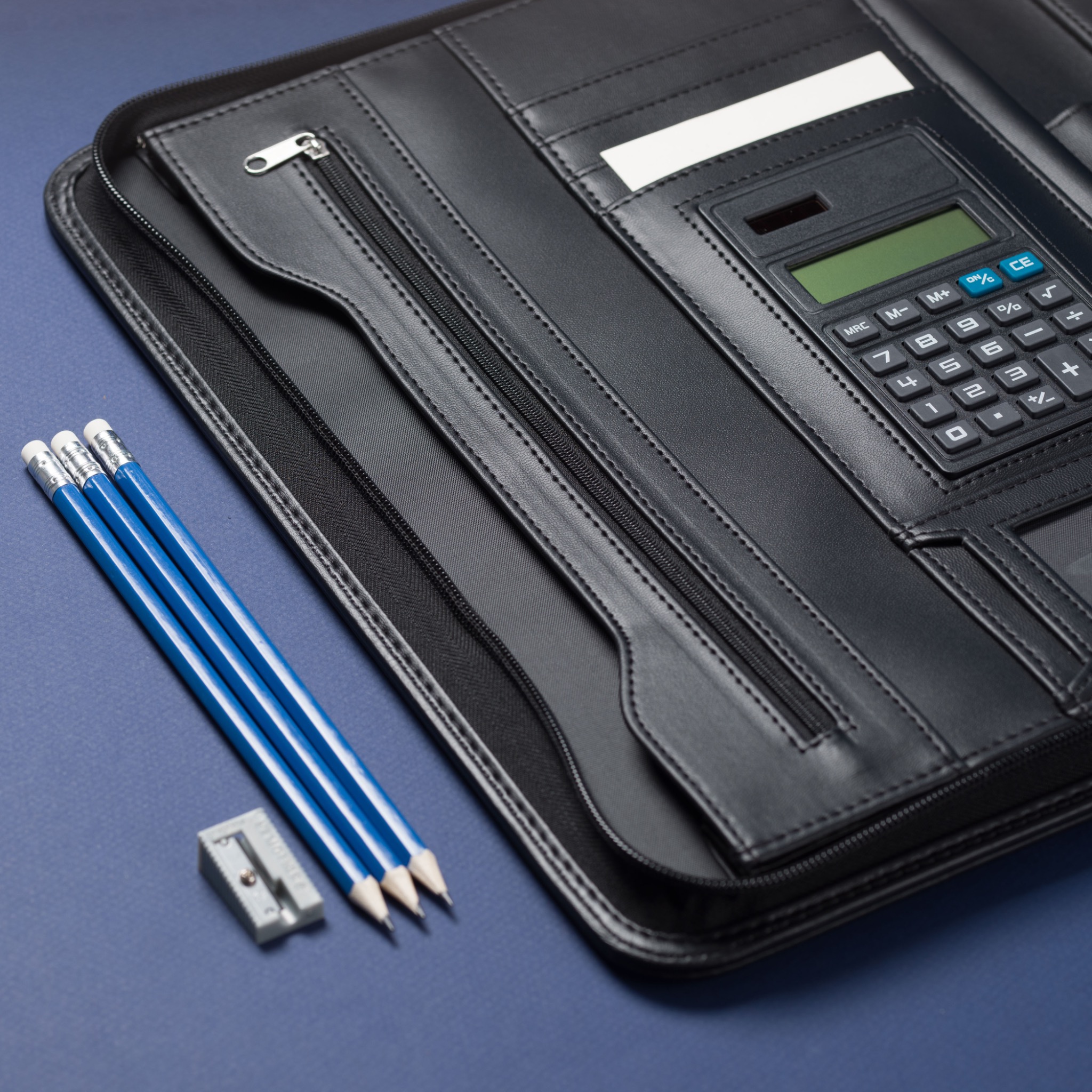 Open black Cossini padfolio styled with blue pencils and an integrated calculator on a blue surface