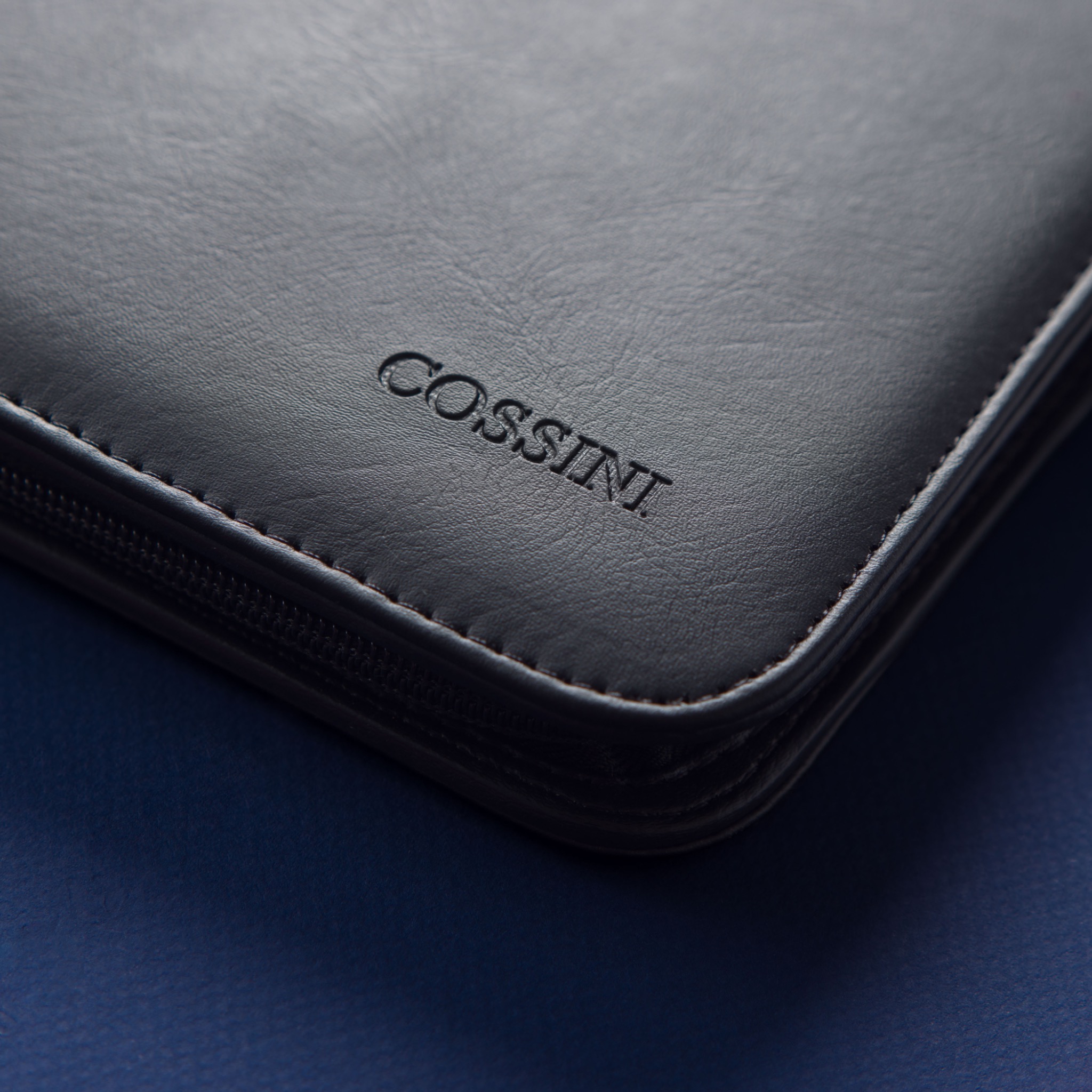 Macro view of the embossed Cossini logo, leather grain, stitching and zipper construction