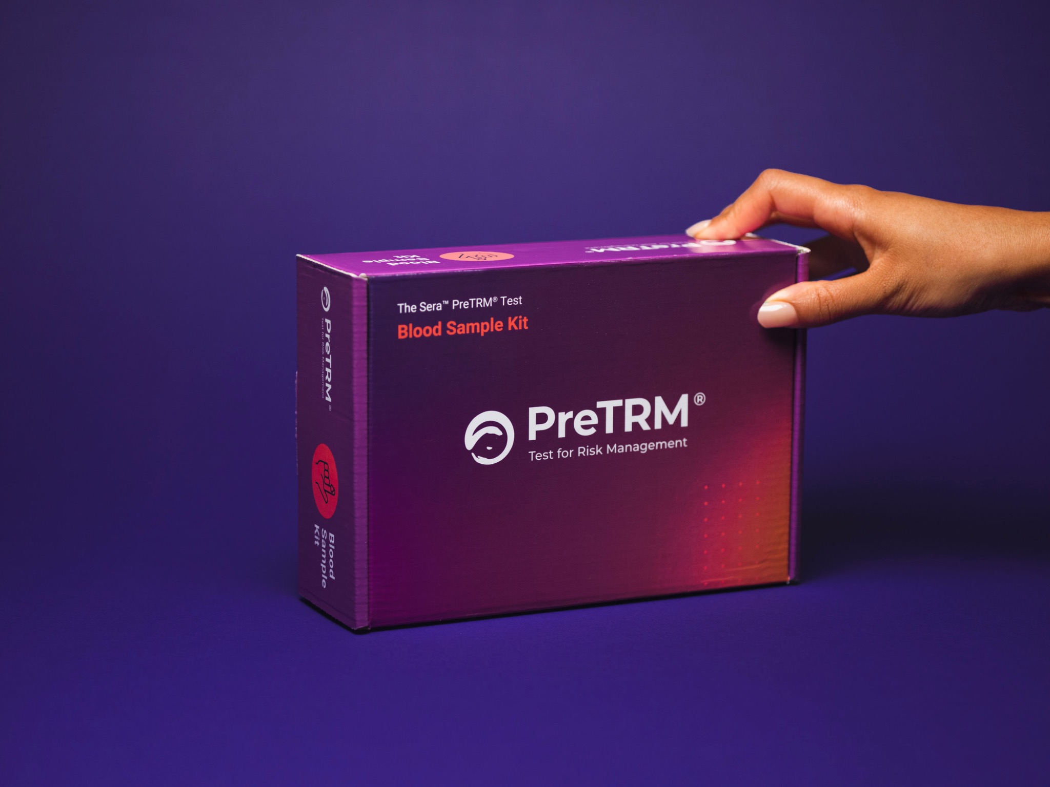 A hand presenting the retouched PreTRM blood sample kit against a deep purple background